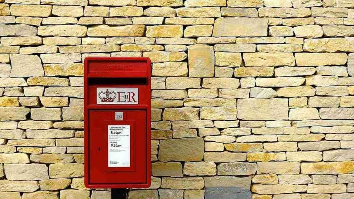 A Royal Mail's red post box stands next to a brick wall