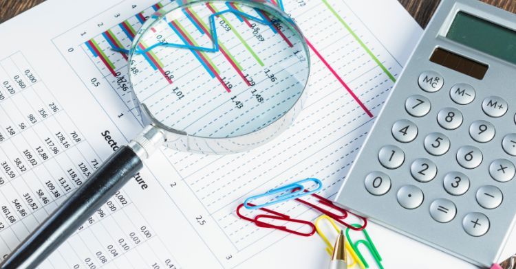 A financial analysis setup with a magnifying glass over a graph a calculator and paper clips on printed sheets