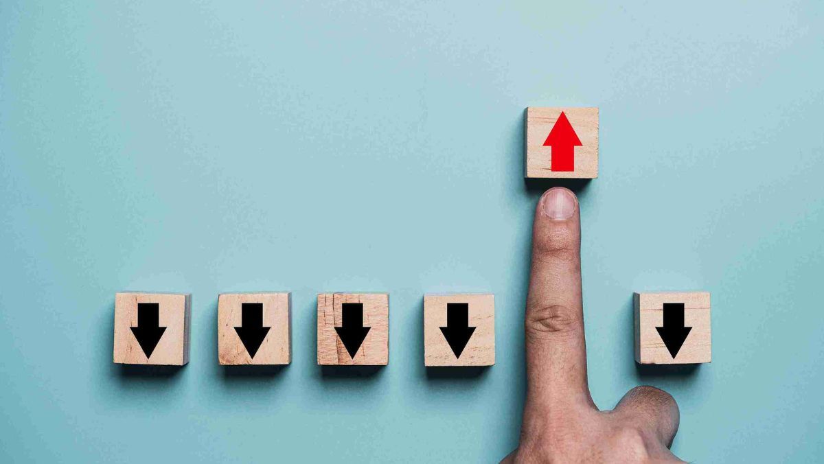 A finger pointing on a block with a red arrow going upward with five other blocks with black arrows pointing downward