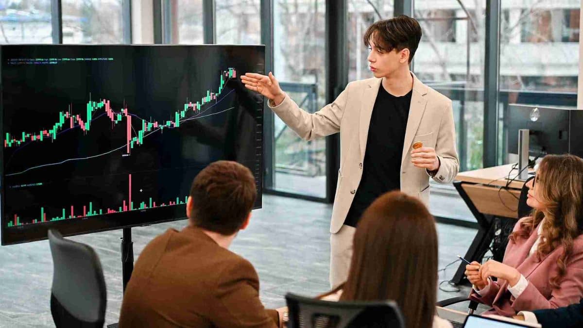 A man confidently presenting a trading chart to a group of people
