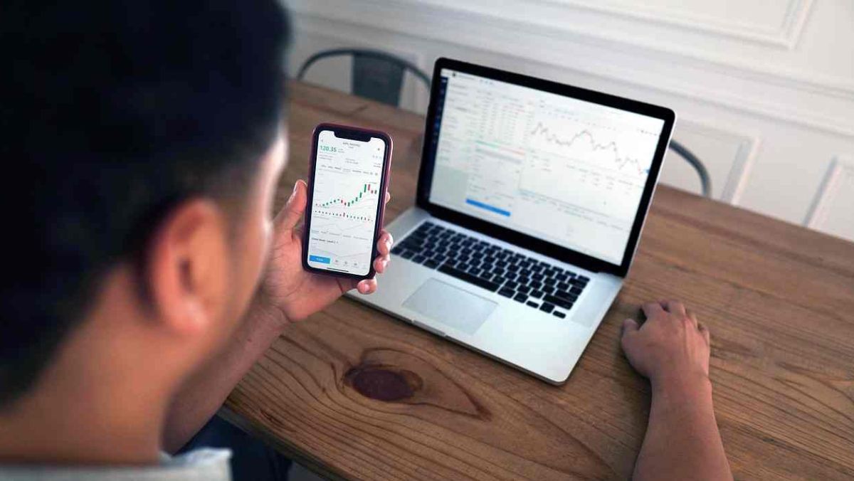 A man holding a mobile phone while a laptop rests on the table