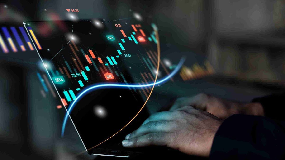 A man is actively engaged in typing on his laptop, displaying trading charts and indicators