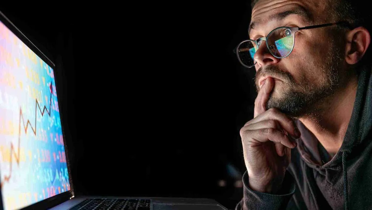 A man with eyeglasses is looking at the computer screen with a curious expression