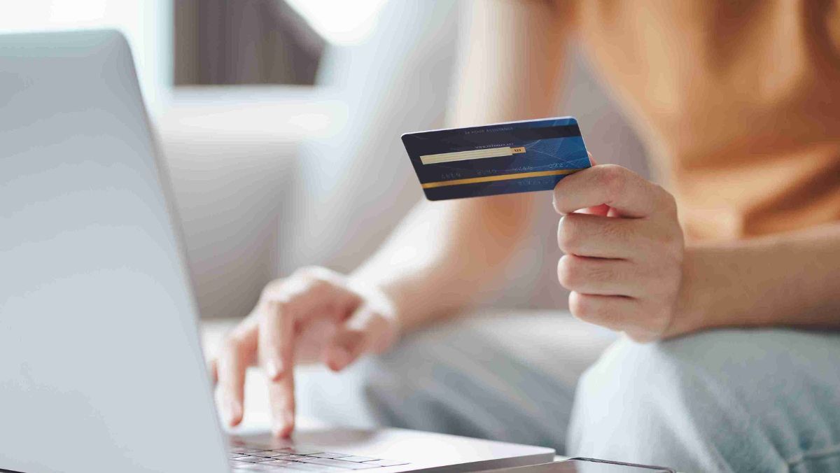 A person holding a bank card while typing on a laptop
