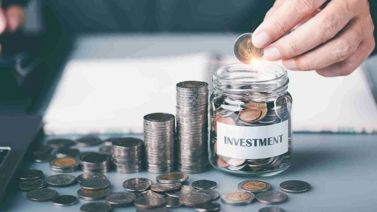 A person places a coin into a glass jar while scattered coins lie outside