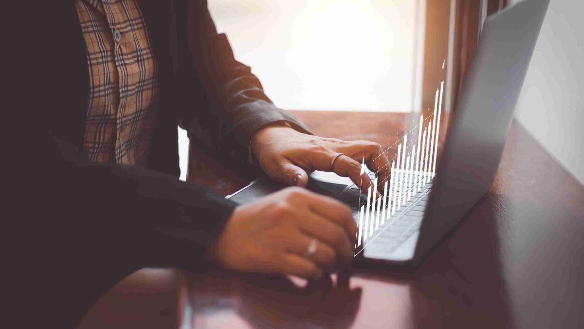 A person using a laptop with holographic bar charts projecting above the keyboard