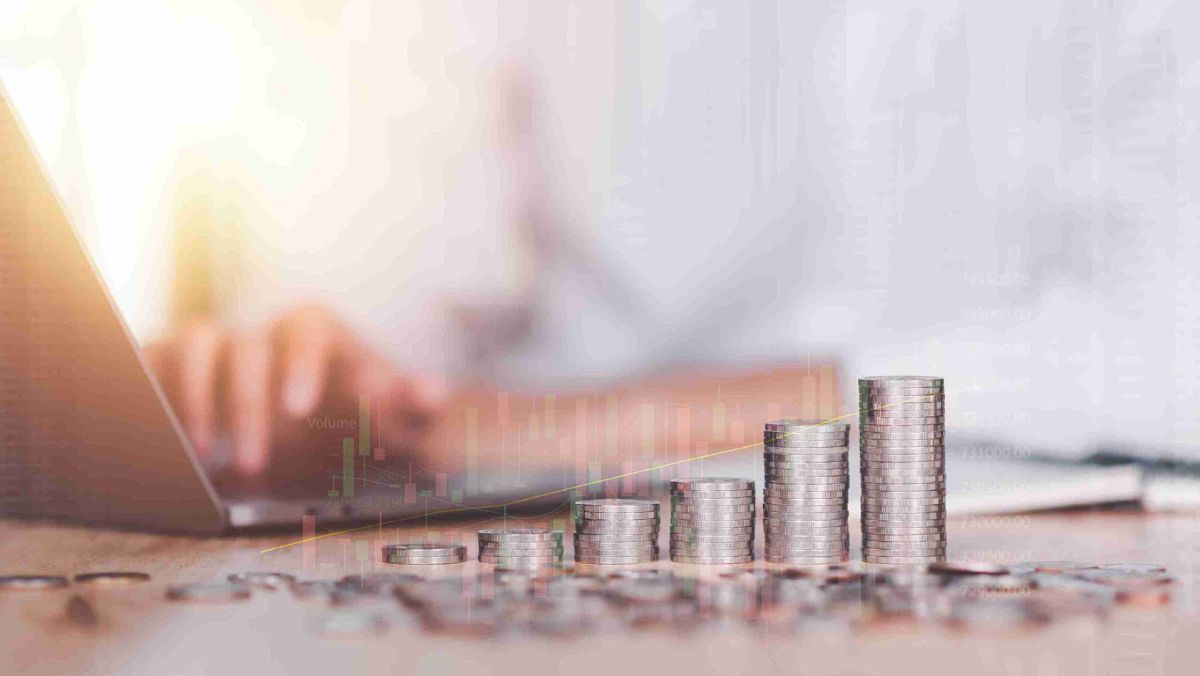 A pile of coins arranged in ascending order, set against the backdrop of a person using a laptop