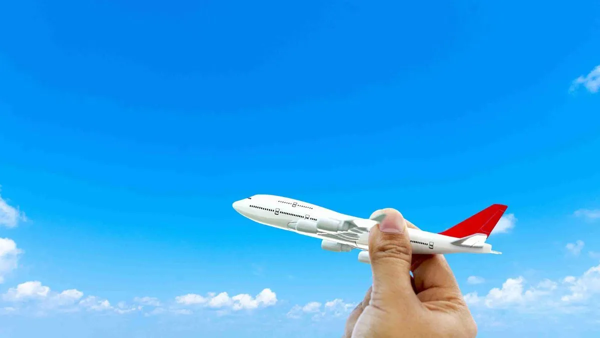 A small toy airplane being held in hand against the backdrop of a clear blue sky