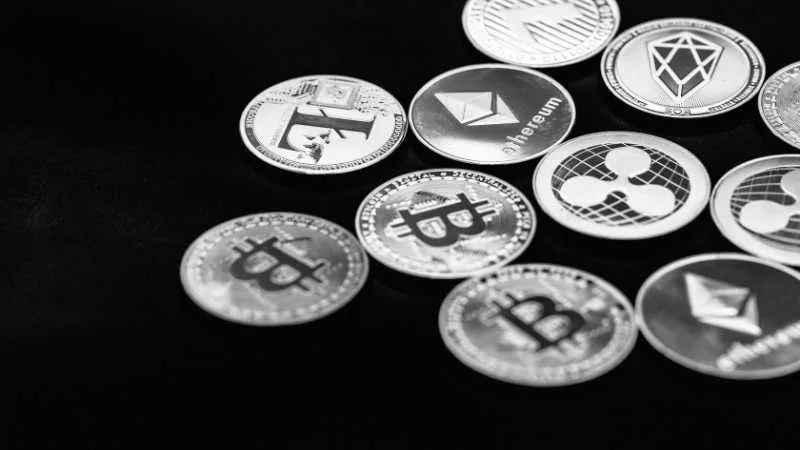 Assorted cryptocurrency coins including Bitcoin and Ethereum in black and white