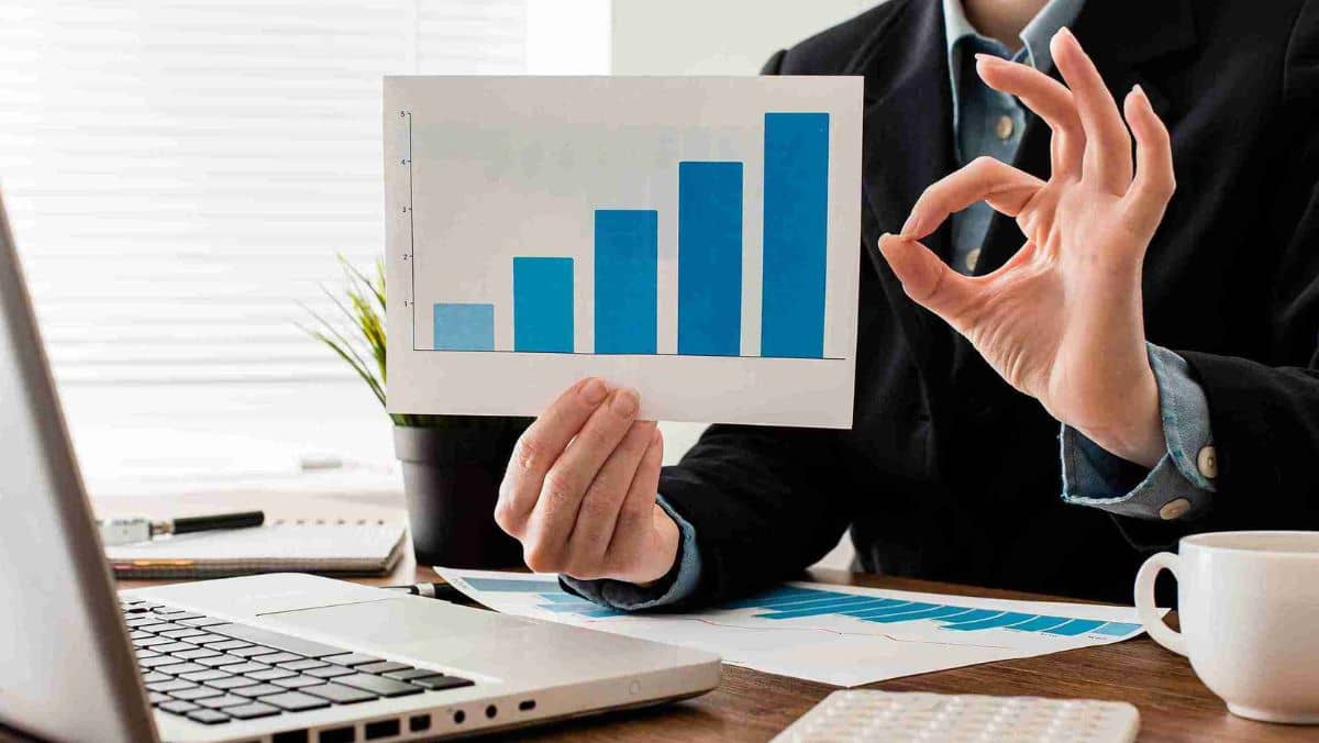 Businessman in an office sitting down doing an ok sign while holding a paper with bar graphs