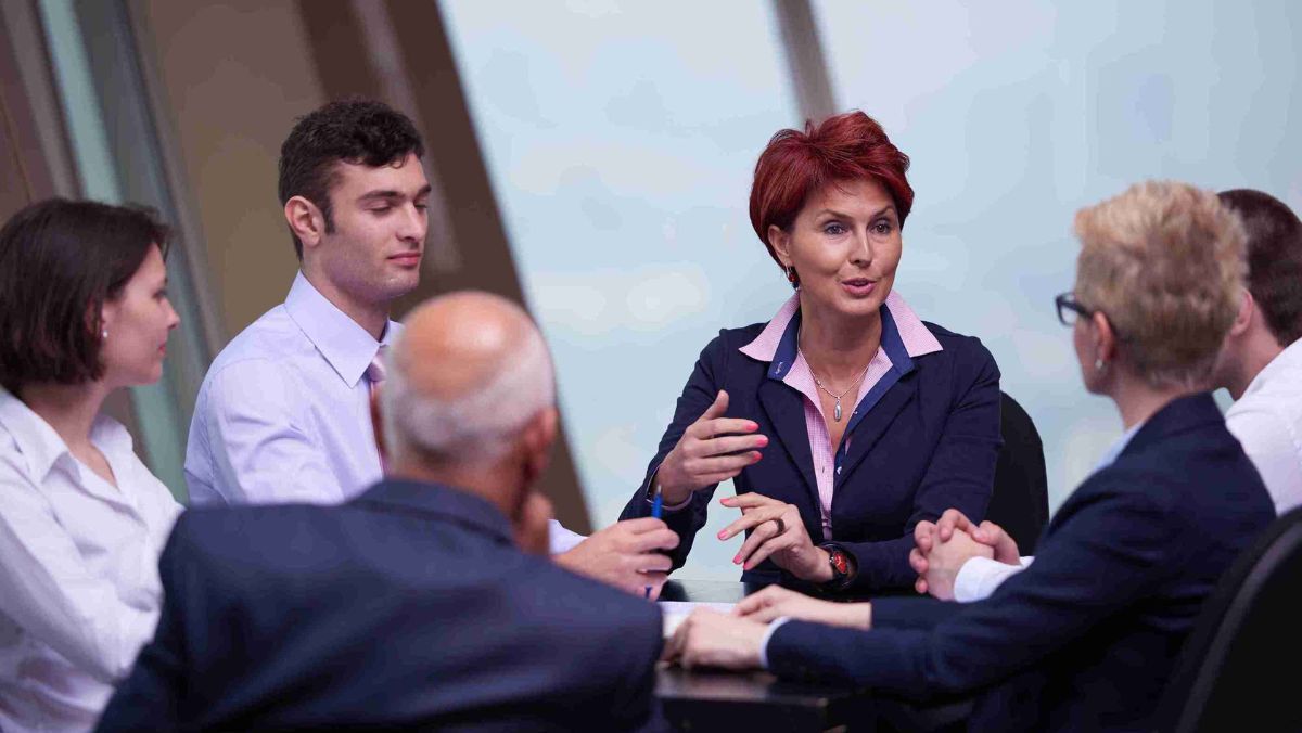 Individuals dressed in professional attire seated in a meeting, engaging in discussion and conversation