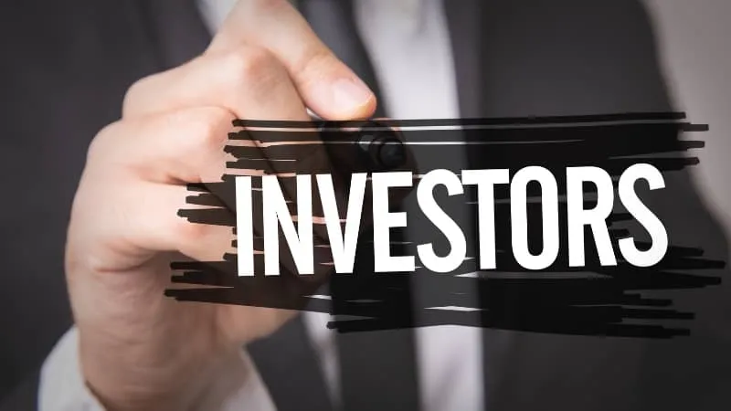 Person writing the word INVESTORS with a marker on a transparent surface