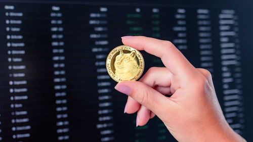 Hand holding a Dogecoin with digital trading data in the background